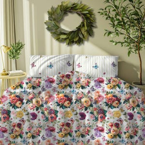 May include: A floral bedding set with a white background and colorful roses, peonies, and butterflies. The pillowcases have a striped pattern with butterflies. A green wreath hangs above the bed, and a small tree is to the right.