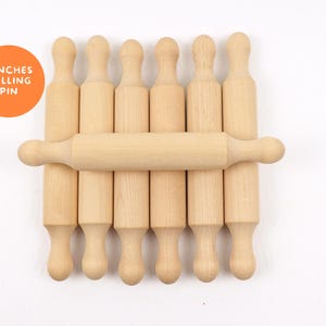 May include: A collection of seven wooden rolling pins, with one horizontal across the others. The rolling pins are light brown and have a classic design. An orange circle with the text "7 INCHES ROLLING PIN" is in the upper left corner.