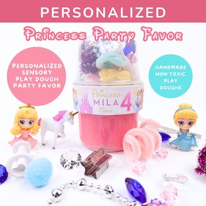 Peut inclure: Un ensemble de cadeaux de fête de princesse personnalisés. L'ensemble comprend un pot de pâte à modeler rose avec le nom "Mila" et le chiffre "4". L'ensemble comprend également des figurines de princesses, une licorne et des accessoires décoratifs.