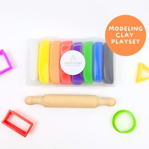 May include: A modeling clay playset with colorful clay sticks, a wooden rolling pin, and various shape cutters. The clay colors include white, yellow, orange, red, purple, green, blue, and gray. The set is designed for creative play.