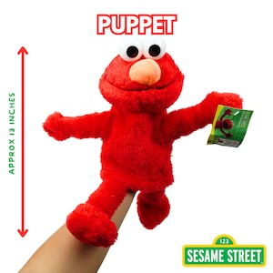 May include: A red Elmo puppet from Sesame Street, approximately 13 inches tall. The puppet has large white eyes, an orange nose, and a tag. The word "PUPPET" is printed above the puppet.