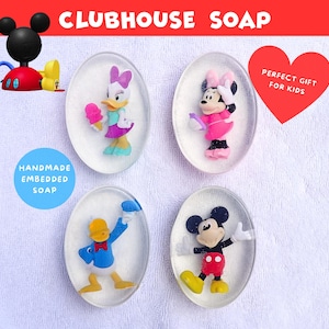 May include: Clubhouse Soap featuring embedded character soaps. The soaps include Mickey Mouse, Minnie Mouse, Daisy Duck, and Donald Duck. The soaps are oval-shaped and clear, with the characters visible inside. The text "Handmade Embedded Soap" is on a blue circle.