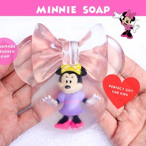 May include: Clear Minnie Mouse-shaped soap with a Minnie Mouse figurine inside. The soap has a pink bow design and the text "MINNIE SOAP" is at the top. A pink circle reads "HANDMADE EMBEDDED SOAP".