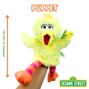 May include: A yellow Big Bird puppet from Sesame Street, approximately 13 inches tall. The puppet has a red beak, blue eyes, and orange and pink striped legs. The word "PUPPET" is printed above the puppet.