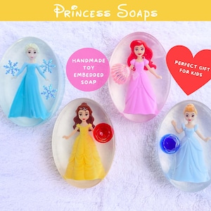 May include: Oval-shaped soaps with embedded princess dolls. The soaps feature dolls in blue, pink, and yellow dresses. The text "Princess Soaps" is at the top. A pink circle reads "Handmade Toy Embedded Soap". A red heart reads "Perfect Gift for Kids".