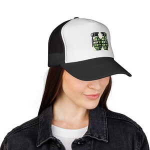 May include: A black and white trucker hat featuring a graphic of two green grenades. The hat has a white front panel with the grenade design, a black peak, and a black mesh back.