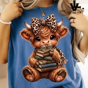 Op de afbeelding: Blauw T-shirt met een cartoon Highland koe ontwerp. De koe heeft een luipaardprint strik, sjaal en bril en houdt boeken vast. Het shirt heeft het VectorLush logo.
