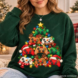 May include: A dark green sweatshirt featuring a graphic of a Christmas tree constructed from various video game controllers, some decorated with reindeer antlers, snowman features, Santa hats, and colourful holiday lights.