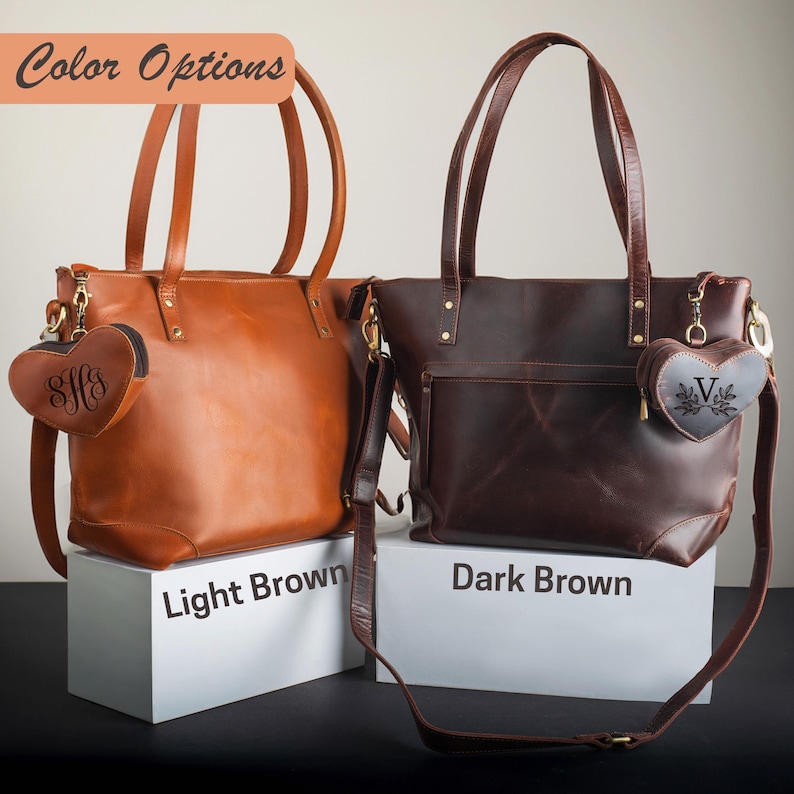 May include: Two leather tote bags in light brown and dark brown, each with a matching heart-shaped charm. The light brown bag has a gold zipper and hardware, and the dark brown bag has a front pocket and a shoulder strap. The text "Color Options" is at the top.