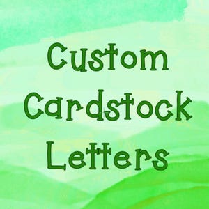 May include: Green text on a watercolor background reads "Custom Cardstock Letters." The letters are a darker shade of green and have a whimsical, playful font. The background is a gradient of light and dark green.