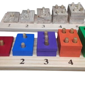 May include: Wooden toy with five colorful blocks, each with a different number of pegs. The blocks are red, blue, purple, orange, and green. The blocks are arranged in a row on a wooden base with numbers 1 through 5.