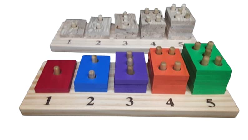 May include: Wooden toy with five colorful blocks, each with a different number of pegs. The blocks are red, blue, purple, orange, and green. The blocks are arranged in a row on a wooden base with numbers 1 through 5.
