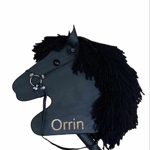May include: Black wooden stick horse toy with black yarn mane and tail. The horse has a black leather bridle with a silver bit and a gold name tag that says "Orrin".