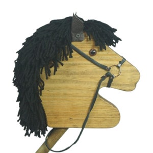 May include: Wooden toy horse head with a black yarn mane and tail. The horse has a brown leather bridle with a metal ring and a brown eye.
