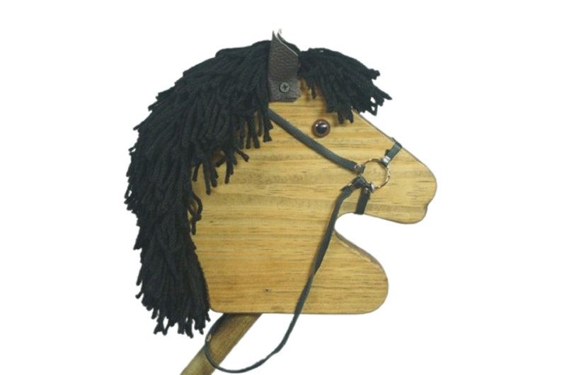 May include: Wooden toy horse head with a black yarn mane and tail. The horse has a brown leather bridle with a metal ring and a brown eye.