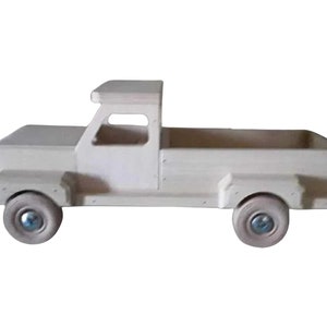 May include: A white wooden toy pickup truck with a flatbed. The truck has a cab with a windshield and a door. The truck has four wheels with black tires and silver hubcaps.