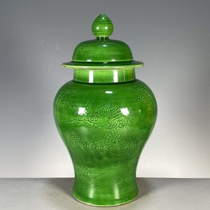 Op de afbeelding: Een felgroene keramische gemberpot met een bijpassend deksel met een puntige knop. Het lichaam van de pot is versierd met een reliëf van een draak en gestileerde wolkenpatronen, afgewerkt met een gladde, glanzende glazuurlaag over het oppervlak.