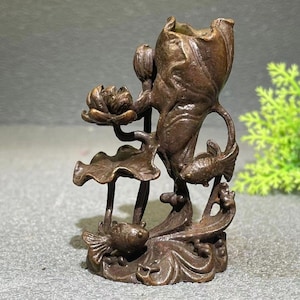 May include: A bronze sculpture depicting a lotus flower, leaves, and two fish. The sculpture has a vase-like shape with intricate details, showcasing a naturalistic design. The color is a dark, aged bronze.