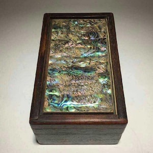 May include: A rectangular wooden box featuring a dark brown finish and a lid inlaid with a large, iridescent abalone shell panel. The shell displays a vibrant, swirling pattern of green, blue, and gold tones, set within a smooth, dark wood frame.