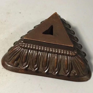 May include: A triangular base with a dark brown finish and a smooth, flat top surface featuring a central triangular cutout. The sides of the base are decorated with a repeating, raised, vertical leaf-like pattern that extends to the bottom edge.