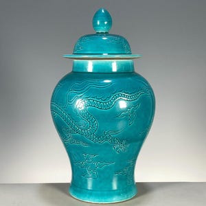 May include: A vibrant turquoise ceramic ginger jar with a matching lid. The vessel features a glossy finish and an embossed design of a long, winding dragon surrounded by stylised clouds that wrap around the entire body of the jar.