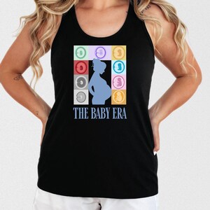 May include: Black tank top with a blue silhouette of a pregnant person in the center. The design includes a square grid of colorful baby icons and the text "THE BABY ERA" in light blue.