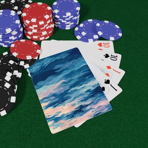 May include: Poker chips in red, black, and blue are stacked on a green surface, alongside a hand of playing cards. The cards show the number 10 in the suits of hearts, spades, and diamonds. One card has a blue and pink abstract design.