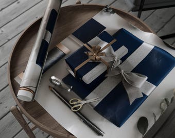 May include: A round wooden table displays wrapped gifts and gift-wrapping supplies. The gifts are wrapped in navy blue paper with silver ribbon and bows. A rolled-up poster, scissors, and a pencil are also on the table.