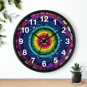 May include: A round wall clock with a black frame. The clock face features a colorful, concentric design with a rainbow of colors. White numbers mark the hours. The clock hands are black.