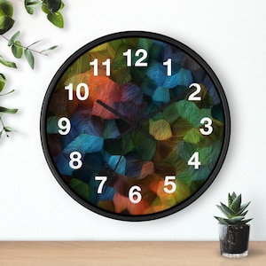 May include: A round wall clock with a black frame and a face featuring a multi-coloured abstract pattern of overlapping strokes in shades of blue, green, orange, and red. The clock has white Arabic numerals from 1 to 12 and two black hands.