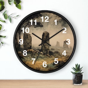 May include: Round wall clock with a black frame featuring a landscape scene with standing stones. The clock face has white numerals and black hands. The background depicts a misty, sepia-toned field with large stone structures.