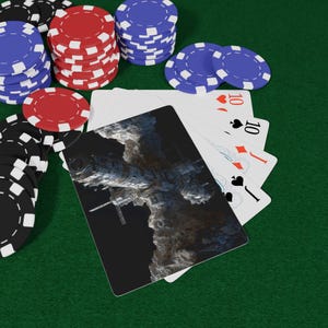 May include: A hand of playing cards featuring a space station illustration on the back, fanned out alongside stacks of red, blue, and black poker chips. The cards display a ten of hearts, ten of spades, jack of diamonds, and jack of spades.