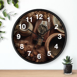 May include: A round wall clock with a black frame. The clock face features a watch, small pottery, and dried plants. White numerals mark the hours. The watch has a silver and gold band. The clock is on a wooden surface.