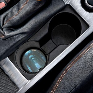 May include: A car cup holder with a coaster featuring a blue and white abstract design. The coaster is placed in the front cup holder. The interior of the car has black leather and silver trim.