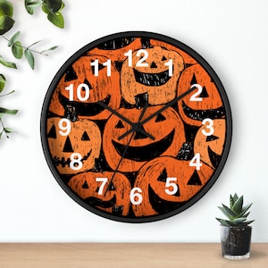 Puede incluir: Un reloj de pared redondo negro con temática de Halloween. La esfera del reloj presenta un patrón repetido de calabazas naranjas con caras negras talladas. Los números blancos marcan las horas. Las manecillas del reloj son negras.
