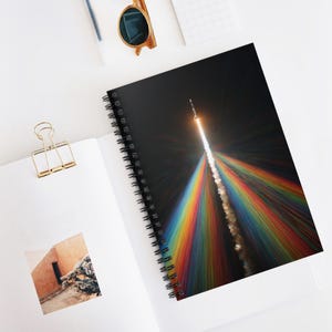 May include: Spiral-bound notebook featuring a vibrant image of a rocket launching into space against a black background. The rocket's trail is depicted as a spectrum of rainbow colors. The notebook is open, revealing blank pages and a gold paper clip.