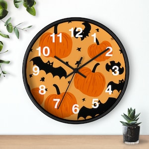 Puede incluir: Reloj de pared redondo con marco negro. La esfera es naranja con ilustraciones de calabazas y murciélagos. Los números de las horas son blancos. Las manecillas son negras.