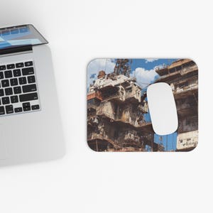 Könnte beinhalten: Ein rechteckiges Mauspad mit einem detaillierten, verwitterten Industriebau-Design und einer weißen Maus. Das Bild zeigt einen Gebäudekomplex mit blauem Himmel im Hintergrund. Das Mauspad befindet sich neben einem Laptop.