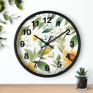 May include: A round wall clock with a black frame and a white face featuring a botanical pattern of yellow sunflowers and green leaves. The clock has black hour, minute, and second hands, and large black numerals from one to twelve.