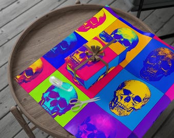 Könnte beinhalten: Eine farbenfrohe Geschenkverpackungsszene mit einer Schachtel, die in Papier mit einem sich wiederholenden Totenkopfmuster in leuchtenden Farben von Pink, Gelb, Blau und Grün verpackt ist. Passendes Geschenkpapier, eine Schere und Klebeband sind ebenfalls sichtbar.