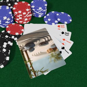 May include: Poker chips in black, red, and blue are stacked on a green felt surface. Playing cards with the number 10 are fanned out. A card with a zen garden scene is in the foreground.