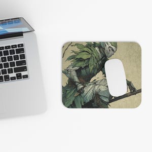 Könnte beinhalten: Rechteckiges Mauspad mit einer detaillierten Illustration eines Fantasy-Charakters mit grüner, blattartiger Rüstung und einer weißen Maus. Der Charakter sitzt auf einem Ast, mit einem neutralen Hintergrund.