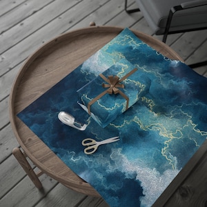 May include: A wrapped gift with a brown ribbon and bow sits on top of a sheet of wrapping paper. The paper has a blue and gold abstract design. A roll of tape and scissors are also on the table, ready for wrapping.