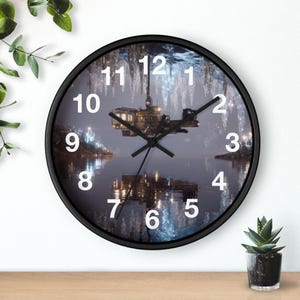 May include: A round wall clock with a black frame and white numbers. The clock face features a detailed image of a structure hovering over a dark, reflective body of water with glowing blue icicle-like formations hanging from above.