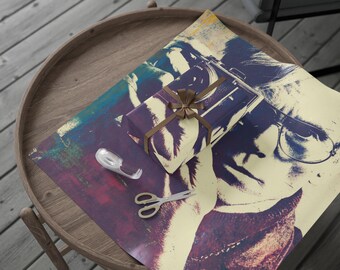 May include: A wrapped gift with a brown ribbon sits on top of wrapping paper with a pop art design. A roll of tape and scissors are next to the gift. The items are on a round wooden table.