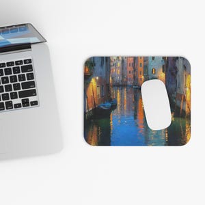 Peut inclure: Tapis de souris rectangulaire avec une peinture colorée d'une scène de canal avec des bâtiments et des bateaux. L'œuvre d'art a une palette de couleurs chaudes avec des reflets dans l'eau. Une souris d'ordinateur blanche est sur le côté droit.