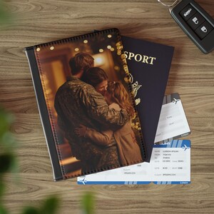 May include: A black leather passport holder with a photo of a couple embracing, a blue passport, and two airline tickets. The tickets display flight information. A car key is also visible.