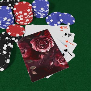 May include: Poker chips in black, red, and blue are stacked on a green surface, alongside playing cards. One card features a dark red rose design. The cards show the ten of hearts, ten of diamonds, and jack of spades.