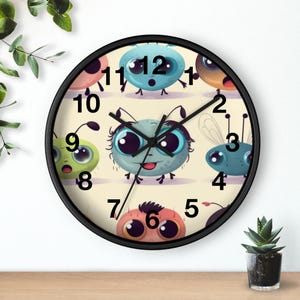 May include: A round wall clock with a black frame and a cream-colored face featuring a pattern of colorful, cartoon-style creatures with large eyes. The clock has black hour, minute, and second hands and black Arabic numerals from one to twelve.