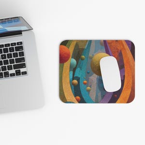 May include: A rectangular mouse mat with a colourful abstract design featuring orange, yellow, blue, and purple curved lines and spheres. A white computer mouse rests on the mat near a laptop.